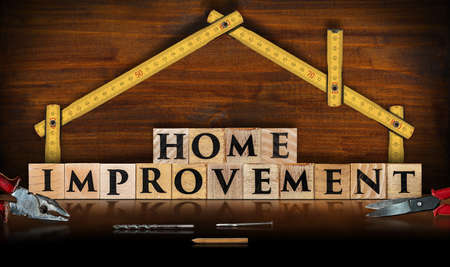Yellow wooden folding ruler in the shape of a house and the text Home Improvement, made of wooden blocks, on a wooden workbench with work toolsの写真素材
