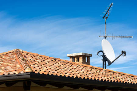 Closeup of a Television Aerial and Satellite Dish on the House Roof on blue sky with cloudsの写真素材