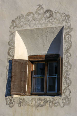 Old wooden window with floral decorations on the white wall in the ancient village of Guarda, Scuol...
