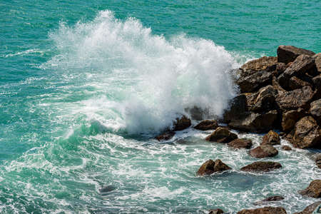 White waves of the green sea break on the rocks. Breakwater in the Gulf of La Spezia, Liguria, Italy