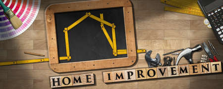 Text Home Improvement made of wooden blocks, work tools, blackboard with folding ruler in the shape of house, calculator and coins, on a parquet floorの写真素材