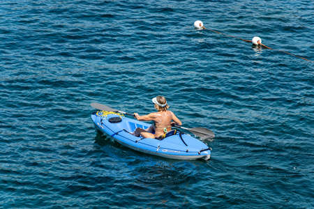 Mature woman aboard a blue kayak, paddling in the blue Mediterranean sea, Gulf of La Spezia, Liguria, Italy, Europe.のeditorial素材