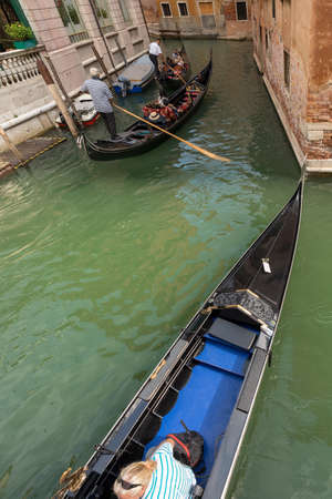 Venice, two gondoliers and tourists on the gondolas, typical Venetian rowing boat. Sightseeing tour along the Canals of the famous city. Veneto, Italy, Europe.のeditorial素材