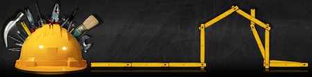 Yellow and orange safety helmet with many work tools and a wooden folding ruler in the shape of...