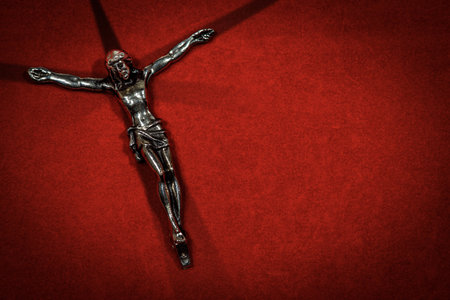 Jesus on the Cross. Closeup of a silver crucifix with cross made of shadows on a red velvet background with copy space.の写真素材