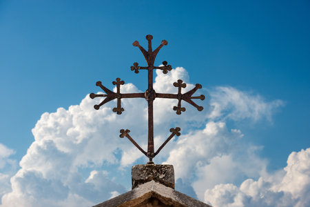 Medieval Christian cross in wrought iron on a blue sky with clouds.