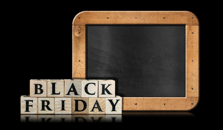 Text Black Friday made of wooden blocks in front of a blank blackboard with copy space. Isolated on black background with reflections.の写真素材