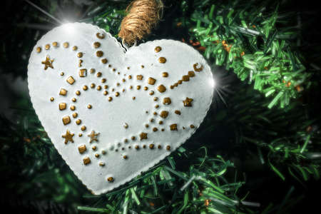Extreme closeup of a white and gold heart hanging on a Christmas tree.の写真素材