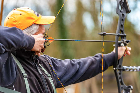 Close-up of a male archer aiming with a hunting compound bow, with blurred vegetation in the background.のeditorial素材