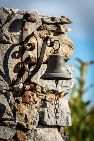 Small bell hanging on a stone wall. Tellaro village, Liguria, Italy, Southern Europe.の写真素材