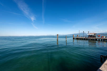 Lago di Garda. Lake Garda from the port of the small town of Lazise with the pier for ferry docking, tourist resort on the coast, Verona province, Italy, Europe. On background the coast of Lombardy.の写真素材