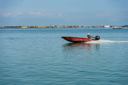 Venice, small red speed boat with one person on board moving in the Venetian lagoon to the Venice islands, the fastest way to travel in this city. Venice, Veneto, Europe.のeditorial素材