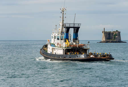 Tug Boat in motion in the Harbor of the Gulf of La Spezia, to the right the ancient Scola Tower...
