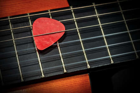 Extreme closeup of a red guitar pick (plectrum) between the strings of the fretboard of an old acoustic guitar. String instrument.の写真素材