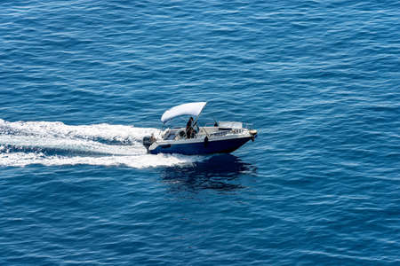 Vernazza, a small blue motor boat with one person on board runs fast in the blue Mediterranean sea...