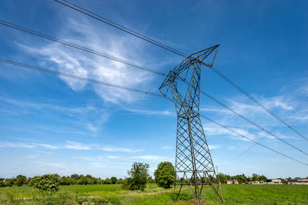 High voltage tower, power line with electric cables and insulators in countryside against a blue sky...