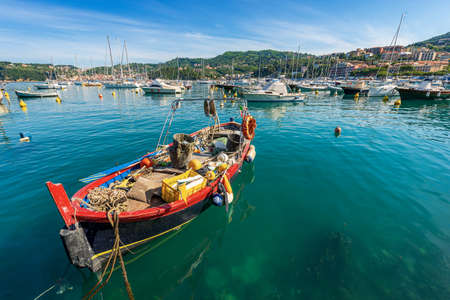 Small red and black fishing boat moored in the port of Lerici town, Tourist resort on the coast of Gulf of La Spezia, Mediterranean sea, Liguria, Italy, Europe. On the left the San Terenzo village.の写真素材