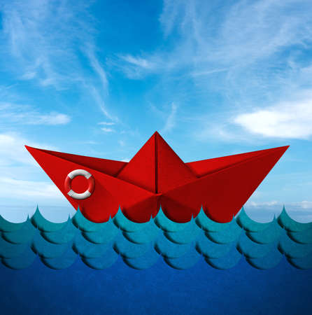 Red paper boat with a white and red lifebuoy in the blue waves of the sea with blue sky and clouds...