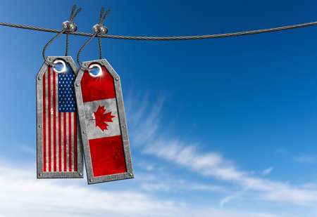 Flags of the United States and Canada against a clear blue sky with clouds and copy space, two metal...