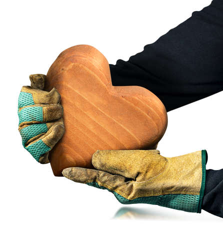 Manual worker with protective work gloves holding a brown wooden heart with copy space, isolated on white background.の写真素材
