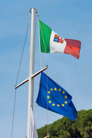 European and Italian flag with emblem of the four Maritime Republics, Venice, Genoa, Pisa and Amalfi hanging on a ship's mast on blue skyの写真素材