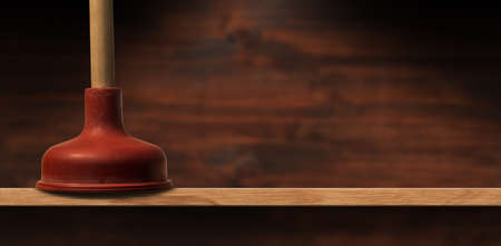 Extreme close-up of a red rubber plunger with wooden handle on a wooden shelf with copy space,...