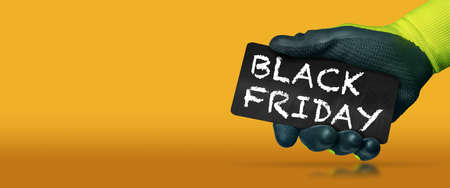 Hand with protective work glove holding a small blackboard with the text Black Friday written in chalk, on a yellow and orange background with copy space and reflections.の写真素材