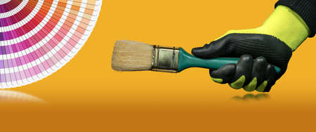 Manual worker with protective work gloves holding a paintbrush on a orange and yellow background with a color swatch guide and copy space.の写真素材