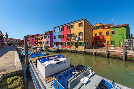 Burano island in the Venetian lagoon with beautiful multi colored houses (bright colors) and a canal with moored boats in a sunny spring day. Venice, UNESCO world heritage site, Veneto, Italy, Europeのeditorial素材