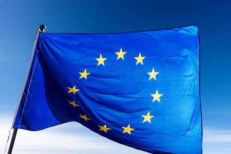 Close-up of an European Union flag waving against a clear blue sky with clouds and copy space.の写真素材