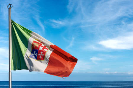 Close-up of the Italian Nautical Flag. Italian flag with emblem of the four Maritime Republics, Venice, Genoa, Pisa and Amalfi on blue sky with clouds and seascape.の写真素材