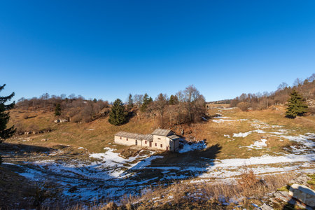 Old stone farmhouse with green and brown pastures in winter. Lessinia Plateau (Lessinia Plateau),...