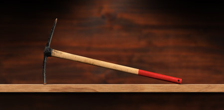 Close-up of a pickaxe or pick ax with red and brown wooden handle on a wooden workbench with copy space. Hand tool used for digging, photography.の写真素材