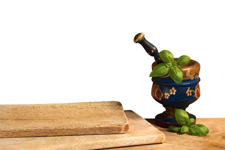 Old wooden mortar and pestle with basil leaves on a wooden table with two cutting boards, isolated on white background, photography.の写真素材