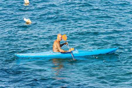 Adult man, 40-45 years, with many tattoos, paddle in the blue Mediterranean sea on a blue kayak. Tellaro village, Lerici, Gulf of La Spezia, Liguria, Italy, Europe.のeditorial素材
