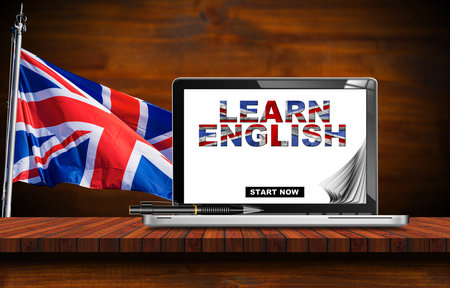 English language lesson. Modern laptop computer with text Learn English in the monitor, on a wooden desk with a UK flag (Union Jack Flag) on background. England.の写真素材
