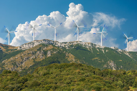 Group of white and blue wind turbines on the top of a mountain range, blue sky with cumulus clouds...