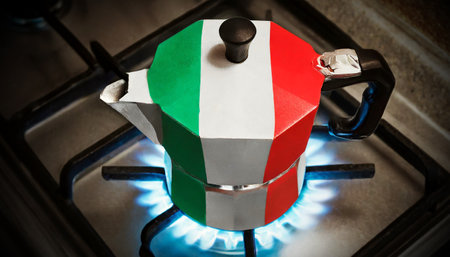 Closeup of a traditional Italian coffee maker (moka or mocha) with the colors of the Italian flag on a kitchen stove with blue flames burning. Generative Ai.の素材