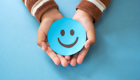 Closeup of a hands of a child (hands cupped,) holding a smiley face made of blue paper on a blue background with copy space. Generative Ai.の素材