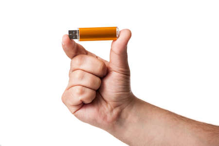 A golden USB memory stick hold between 2 fingers isolated on a white background