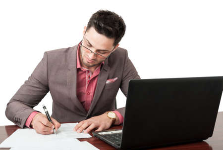 Young and handsome manager signing business documents on his desk on his office with an open laptop near himの写真素材