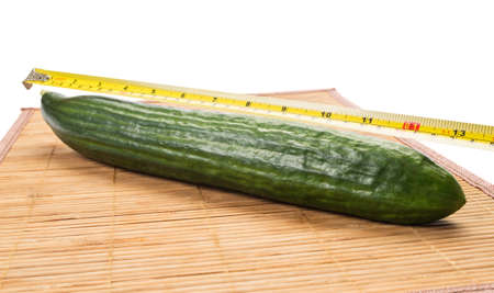 Big yellow centimeter measuring a big fabio cucumber on a bamboo plate with white backgroundの写真素材
