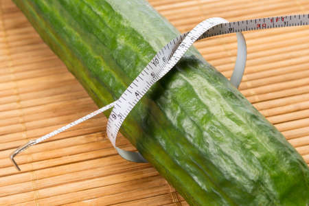 Closeup with a white centimetter measuring a big green cucumber on a bamboo tableの写真素材