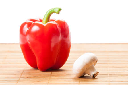 One red pepper and single champignon mushroom on bamboo plate and white backgroundの写真素材