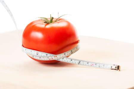 Measure calories of a perfect red tomato with a centimeter. Diet concept made of tomato, meter, wooden board and white background.の写真素材