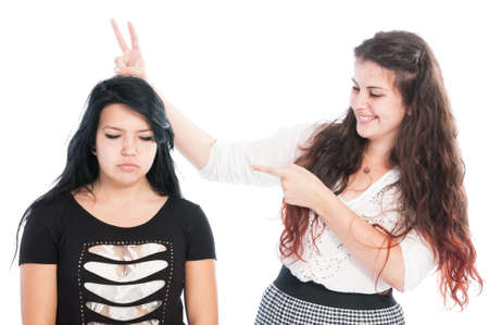 Bully girl making rabbit ears. Bullying concept between girls isolated on white backgroundの写真素材