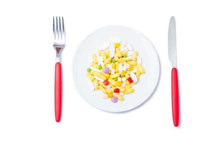 Bunch of colored pills on a white plate with knife and forkの写真素材