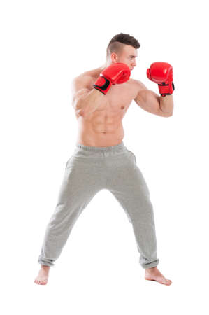 Young and strong, muscular guy wearing red boxing gloves and sporty pants on white backgroundの写真素材