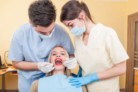 Hygienist working with assistant on a beautiful woman patient with perfect teethの写真素材