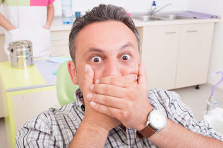 Scared man at dentist covering his mouth. Pain in dental office concept or ideaの写真素材